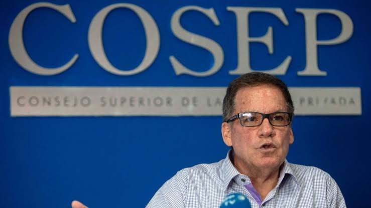Un hombre habla ante micrófonos con un fondo azul que dice COSEP