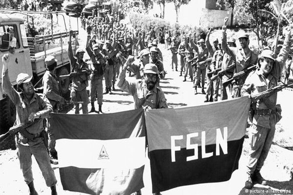 Hombres armados desfilan por una calle detrás de una bandera rojinegra del FSLN