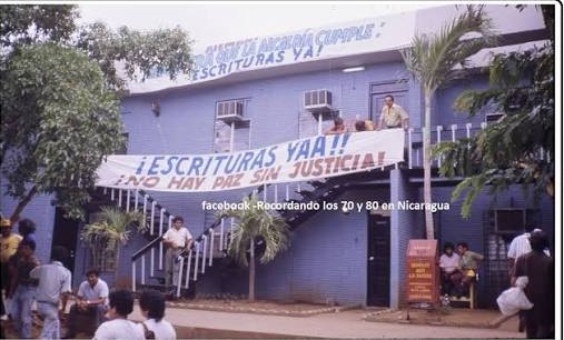 Edificio de la Alcaldía de Managua con una pancarta que pide escrituras y personas sentadas en la entrada