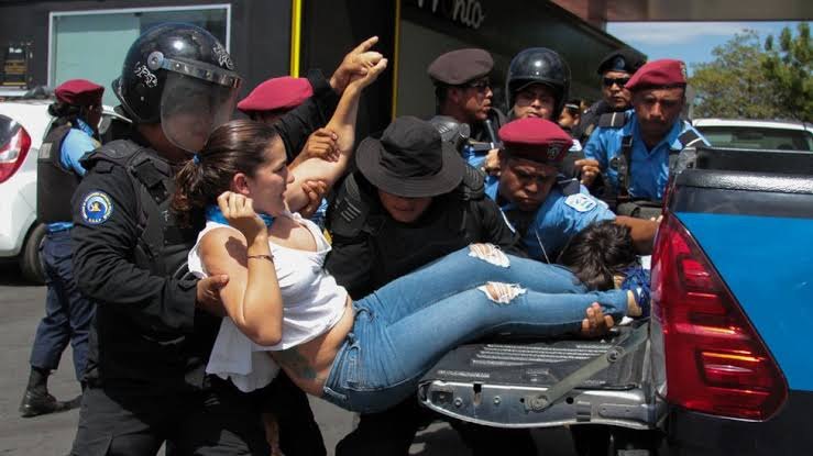 Policías y hombres con boinas rojas suben a una mujer a la caja de una camioneta