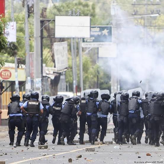 Fila de policías antidisturbios avanza entre humo y piedras en una avenida