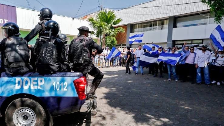 Policías sobre una camioneta de la DOEP frente a manifestantes con banderas