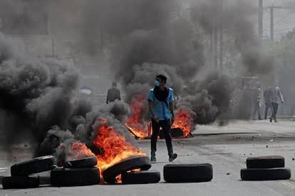 Barricada de llantas en llamas con una persona de pie al fondo