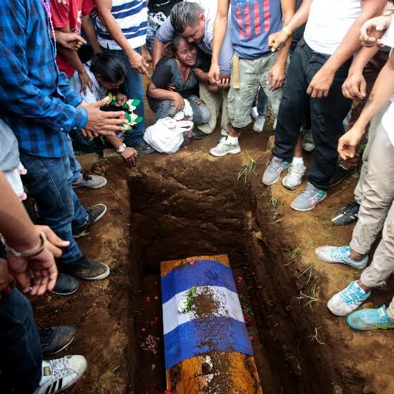 Un entierro: un ataúd cubierto con la bandera de Nicaragua en la fosa, rodeado de personas