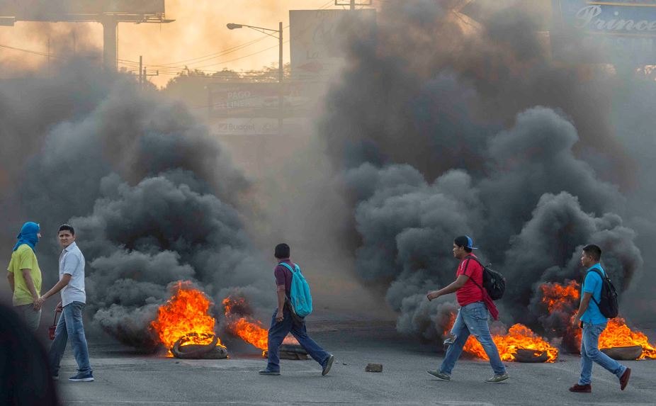 Barricadas en llamas y humo negro; varias personas caminan por la calle