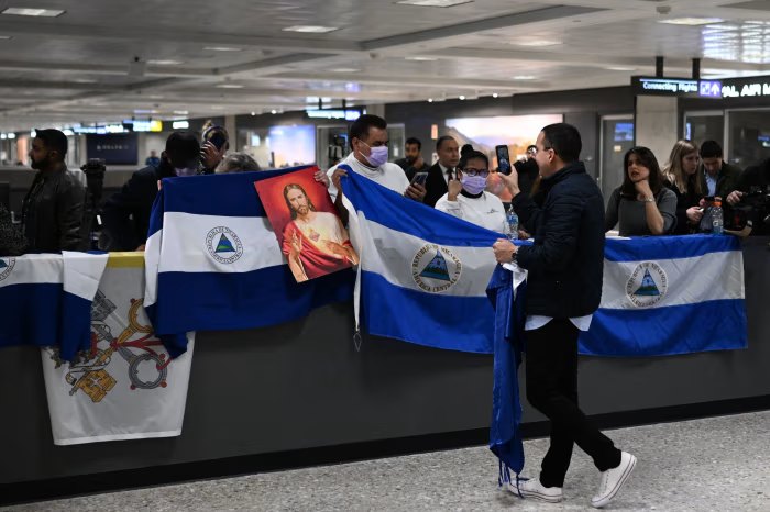 Personas con banderas de Nicaragua y una imagen religiosa en un aeropuerto