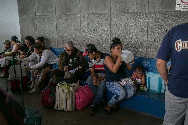 Personas con maletas y bolsos sentadas en una banca de una terminal