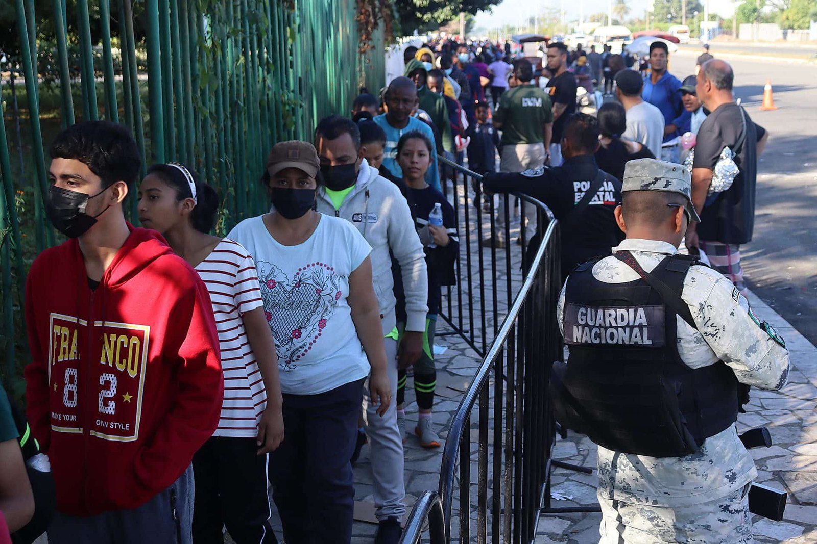 Personas con mascarilla hacen fila junto a un agente de la Guardia Nacional